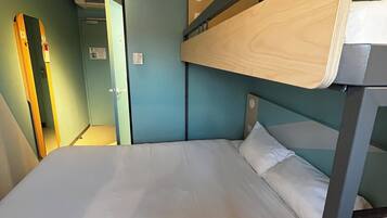 A bunk bed with a wooden headboard, a white mattress, and a light-colored blanket. There is a wall-mounted air conditioning unit above the bed and a door to the left.