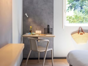 A modern room with a desk, chair, and a window with a view of greenery. - Ibis Budget Bourg-En-Bresse (Bourg-en-Bresse)