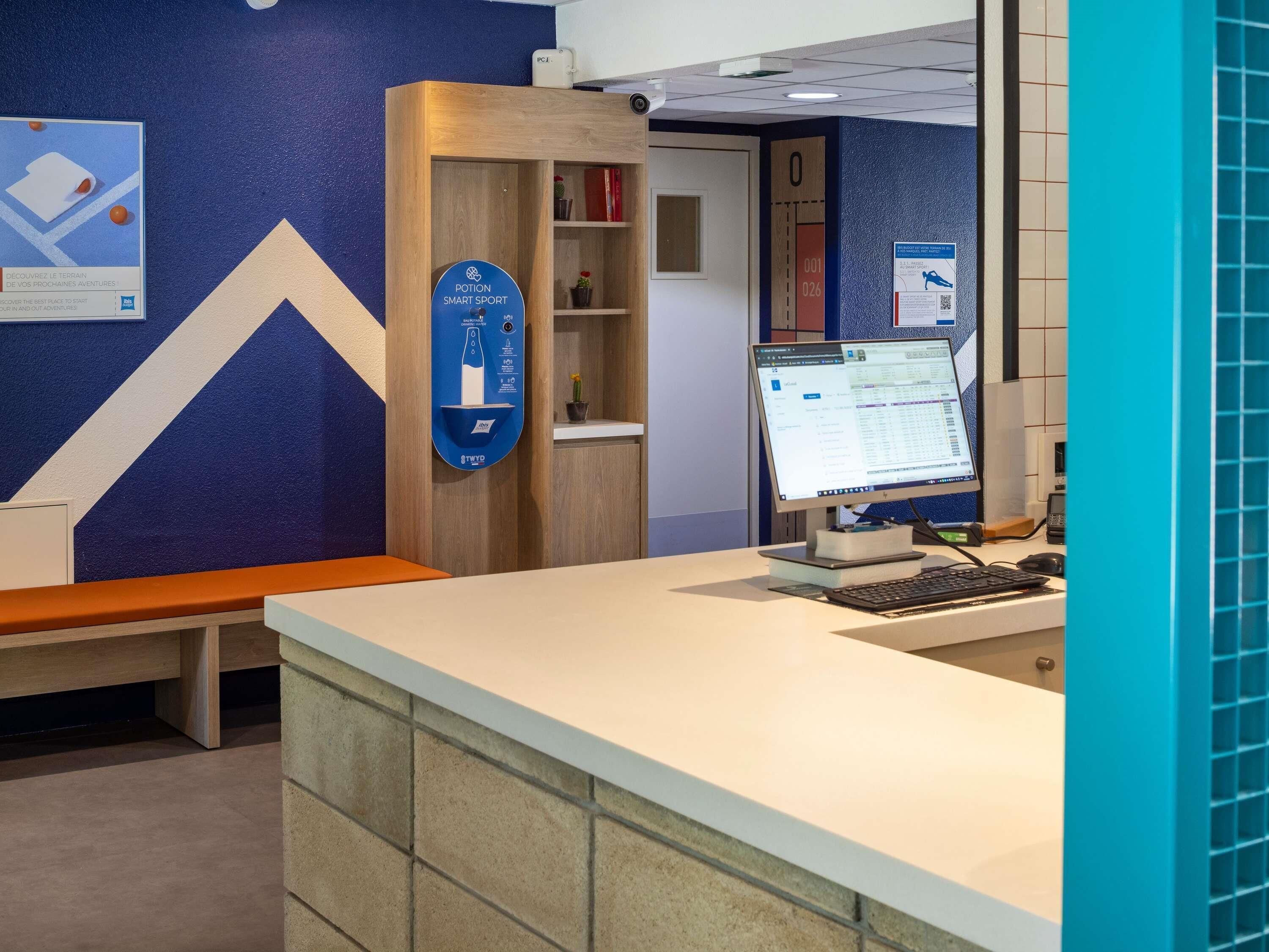 Un comptoir d’accueil avec un écran d’ordinateur, une enseigne indiquant « Potion Smart Sport », et un mur bleu orné d’un motif géométrique.