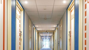A hotel hallway with doors marked with room numbers, a patterned carpet, and a ceiling with recessed lighting. - Ibis Budget Bourg-En-Bresse (Bourg-en-Bresse)