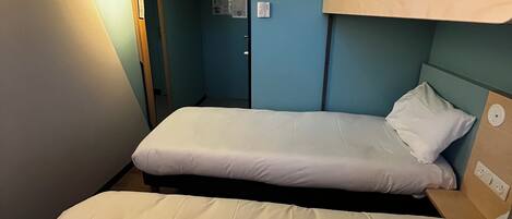 Une chambre avec un lit superposé, un lit simple en bas et un autre lit superposé en haut. Il y a une porte sur la gauche et un appareil de climatisation fixé au mur.