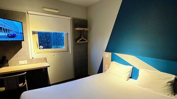 Una habitación de hotel con cama, escritorio, silla, televisor y ventana.