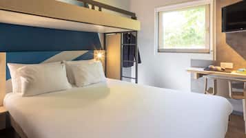 Quarto de hotel com beliche, escrivaninha com cadeira, televisão e janela com vista para o verde.