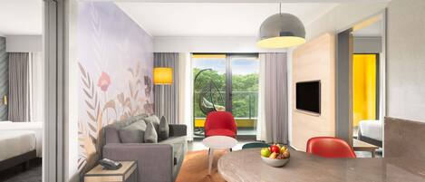 A modern hotel room with a sofa, dining table, and a balcony with a view of greenery.