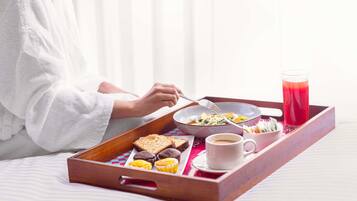 A breakfast tray with toast, muffins, a bowl of salad, a cup of coffee, and a glass of red juice on a bed.