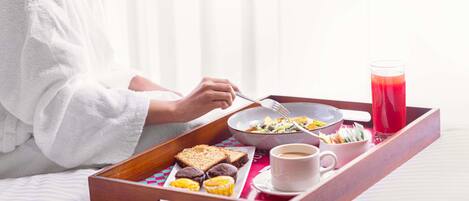 A breakfast tray with toast, muffins, a bowl of salad, a cup of coffee, and a glass of red juice on a bed.