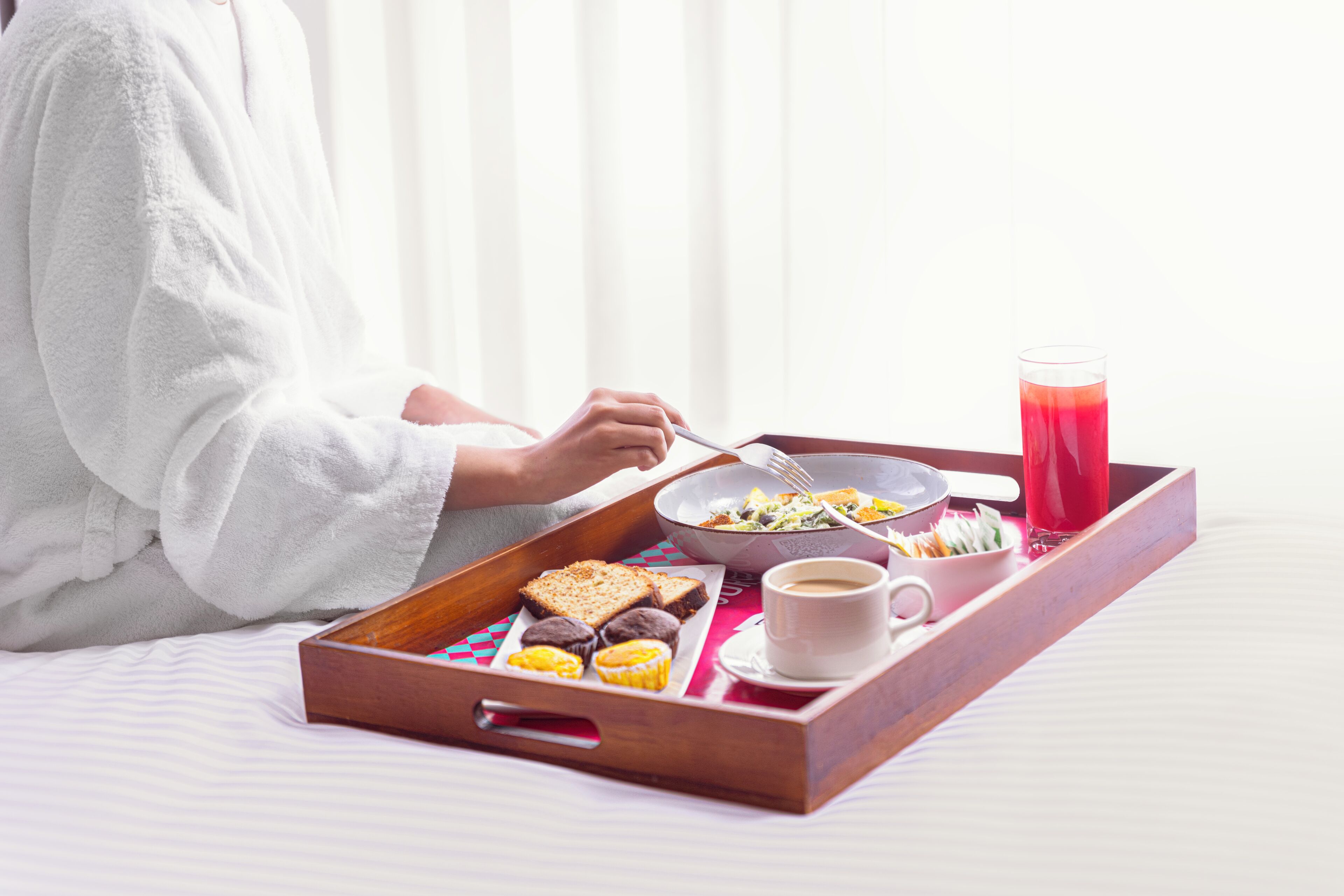 A tray with breakfast items including toast, muffins, and a cup of coffee, set on a bed with a white bedspread.