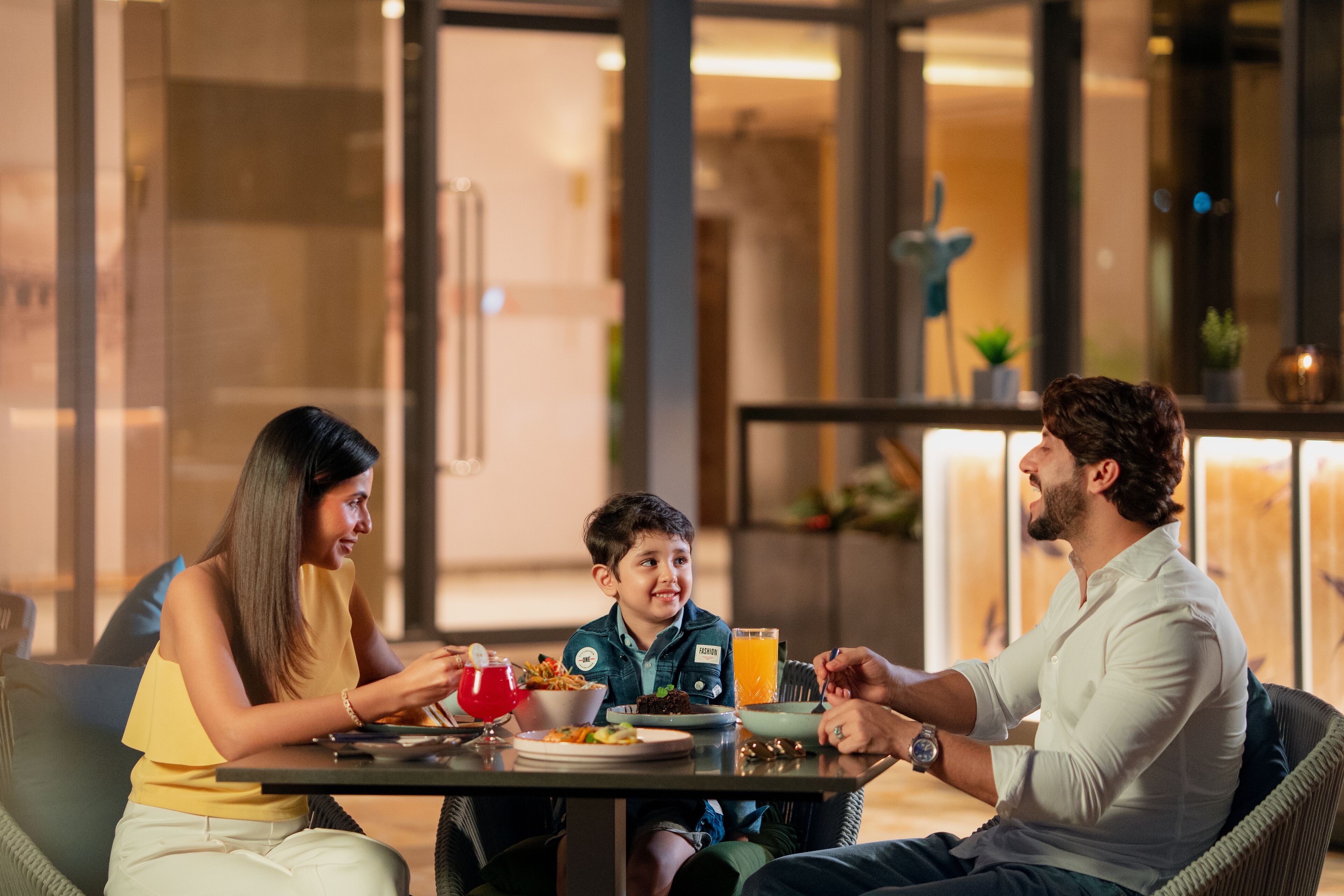 A family dining at a table with a glass of orange juice, a bowl of food, and a red drink.