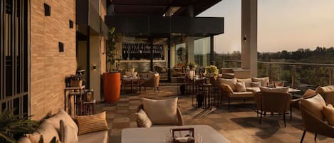 A modern outdoor seating area with a bar, cushioned seating, and a view of the landscape.