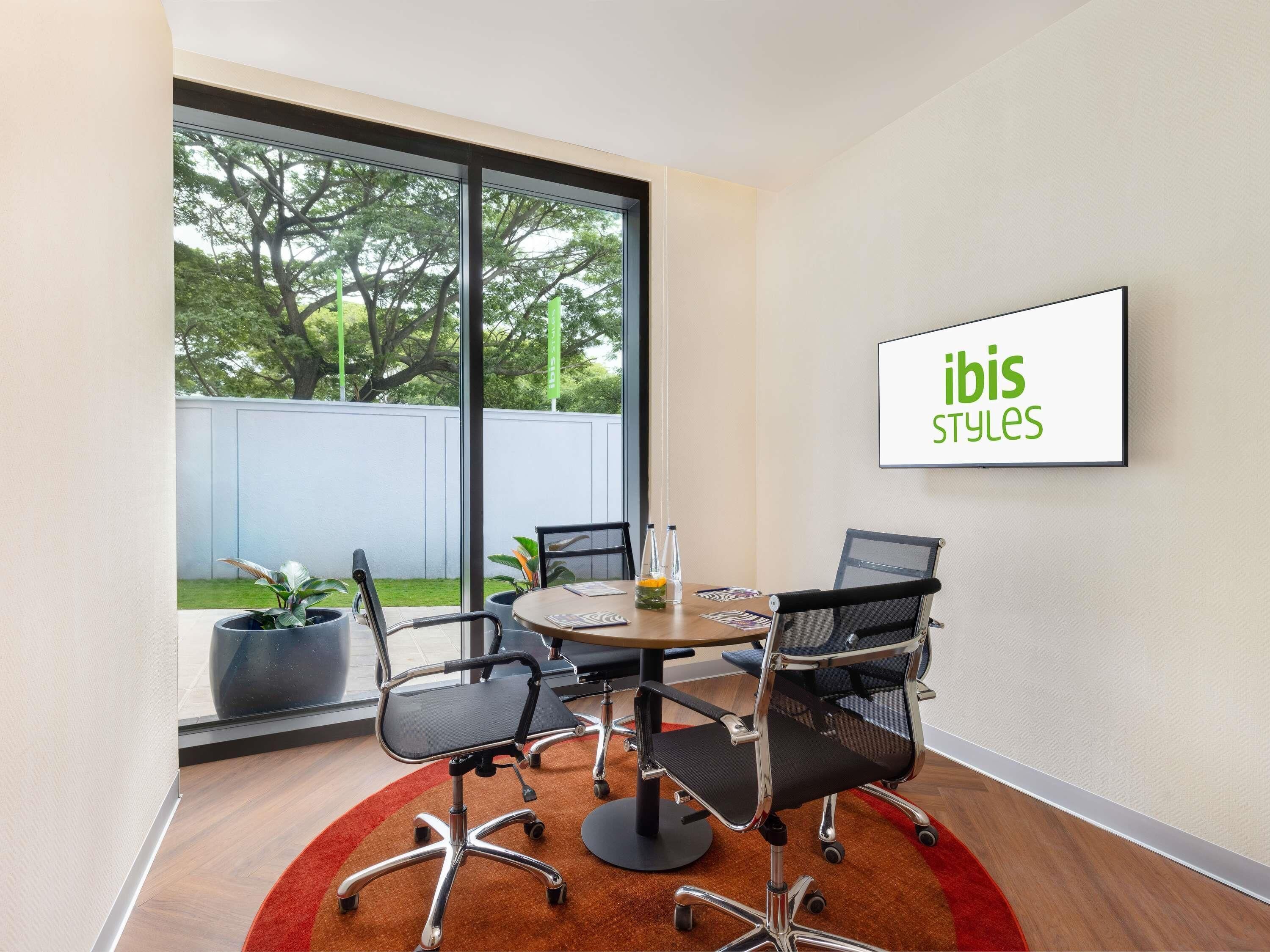 A conference room with a large window, a round table, and four office chairs.