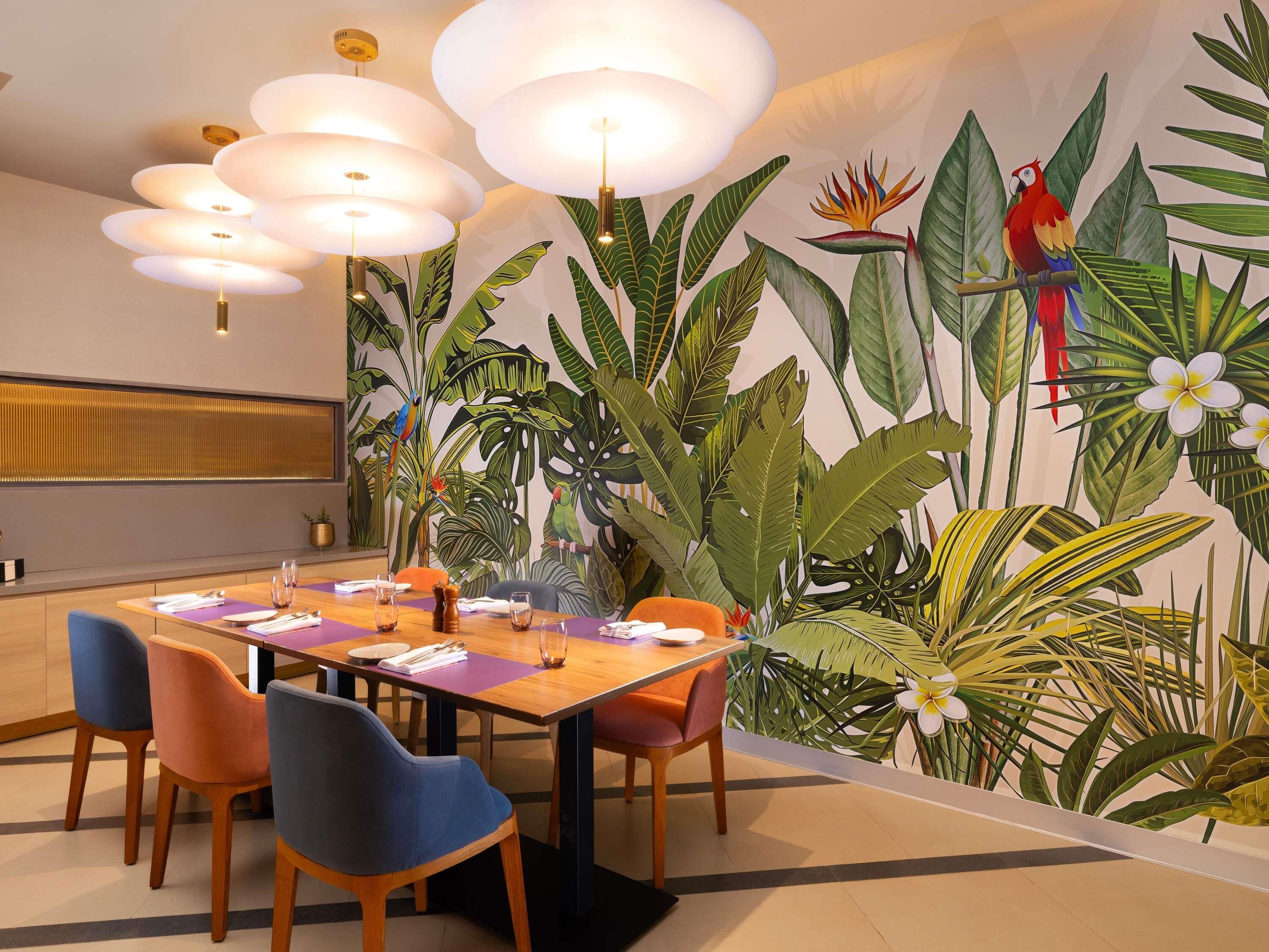 A dining area with a wooden table, chairs, and a mural of tropical plants and birds.