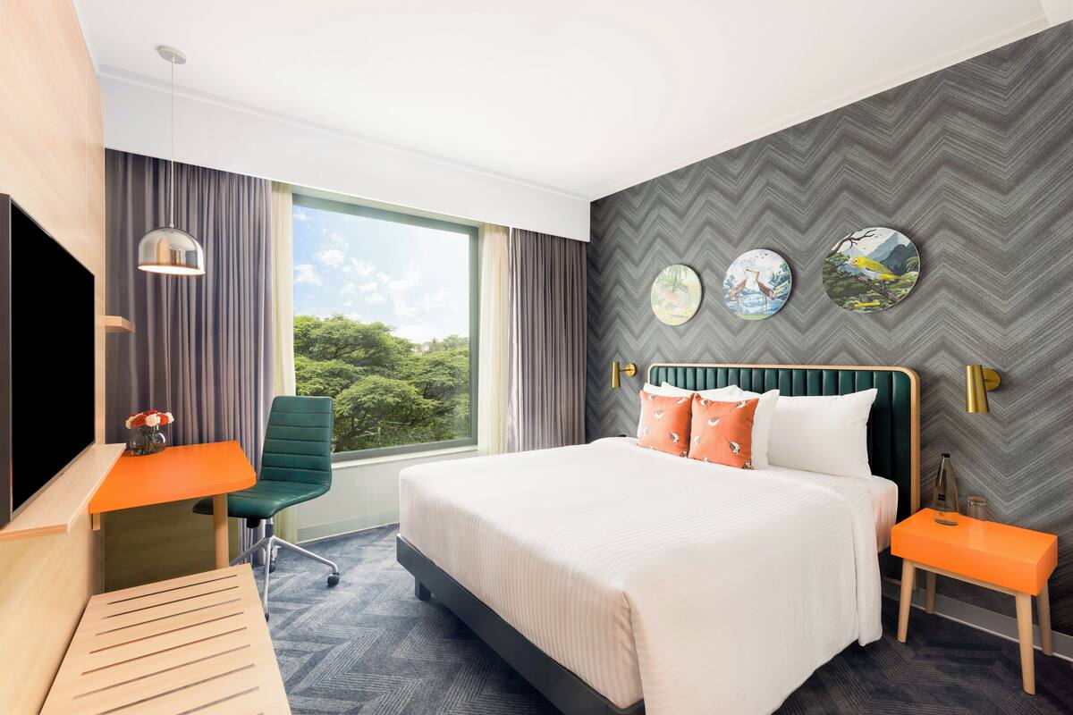 A modern hotel room with a large bed, a desk, a chair, and a TV.