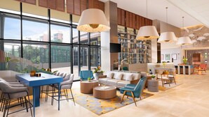 Eine großzügige Lobby mit einer Rezeption, einer Sitzecke und einem großen Fenster mit Blick ins Freie.