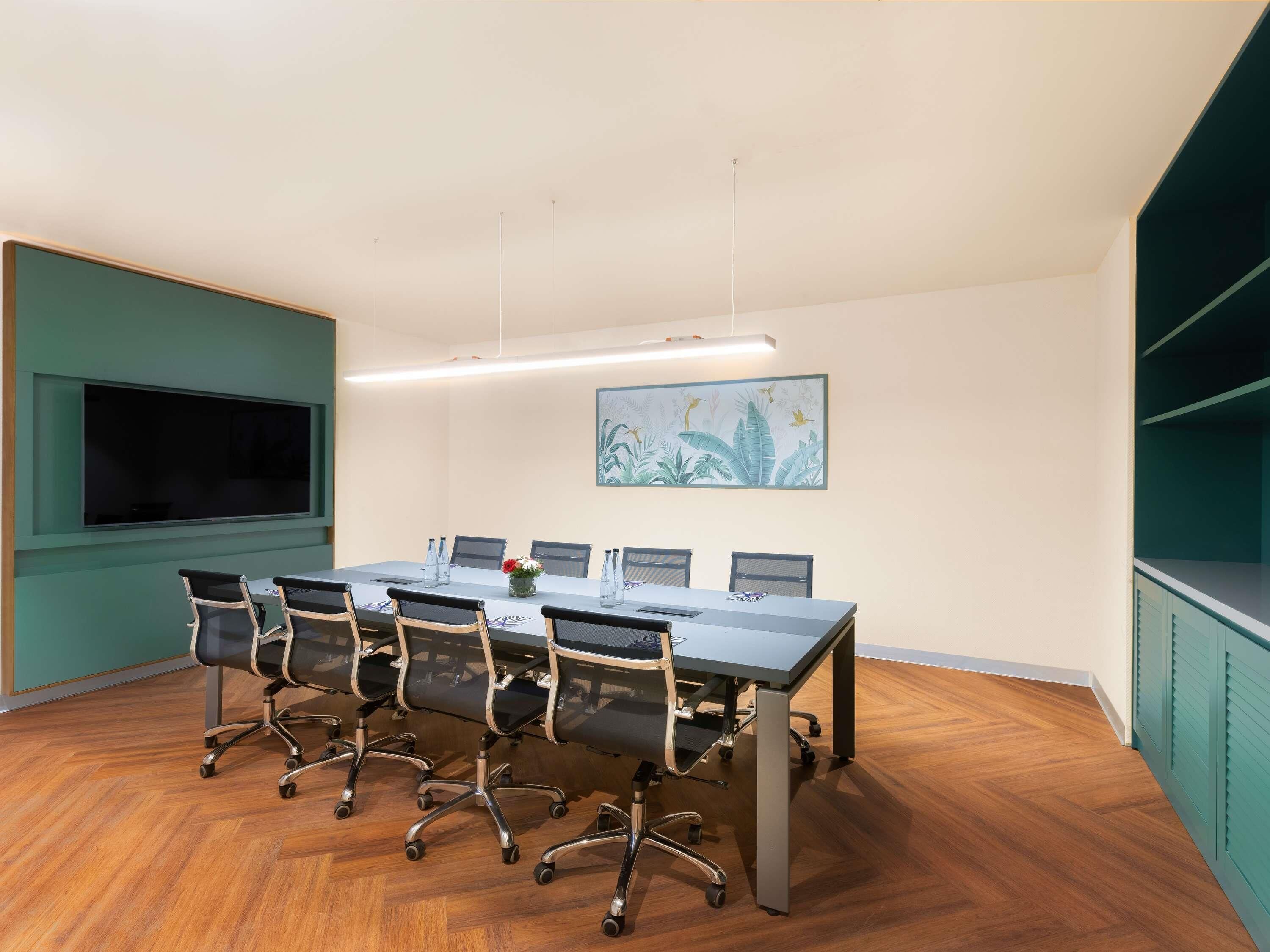 Une salle de conférence avec une longue table, des chaises, un écran de télévision et un tableau accroché au mur.
