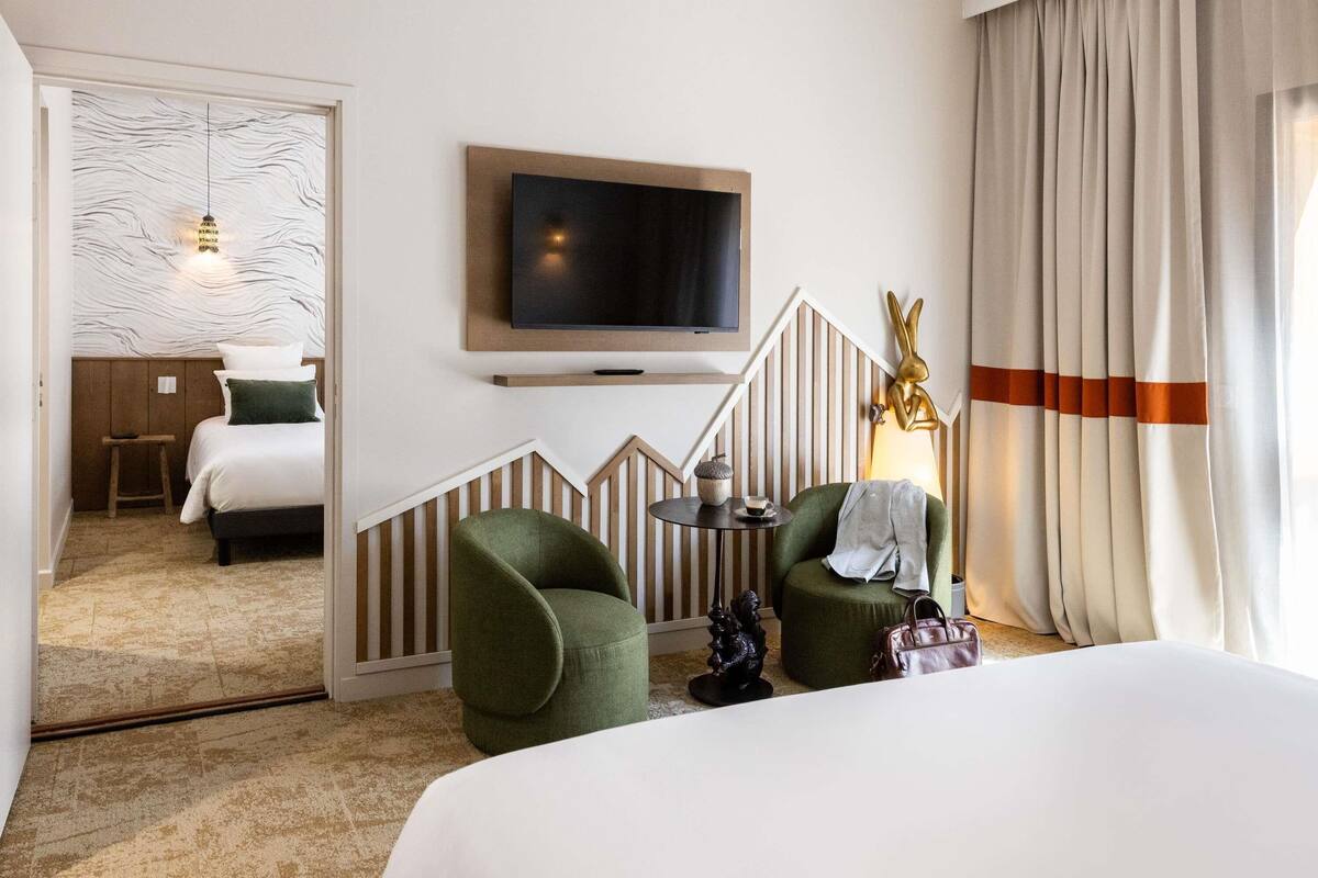 Ein Hotelzimmer mit einem Bett, einem Fernseher, einem grünen Sessel, einem kleinen Tisch und einer dekorativen Lampe.