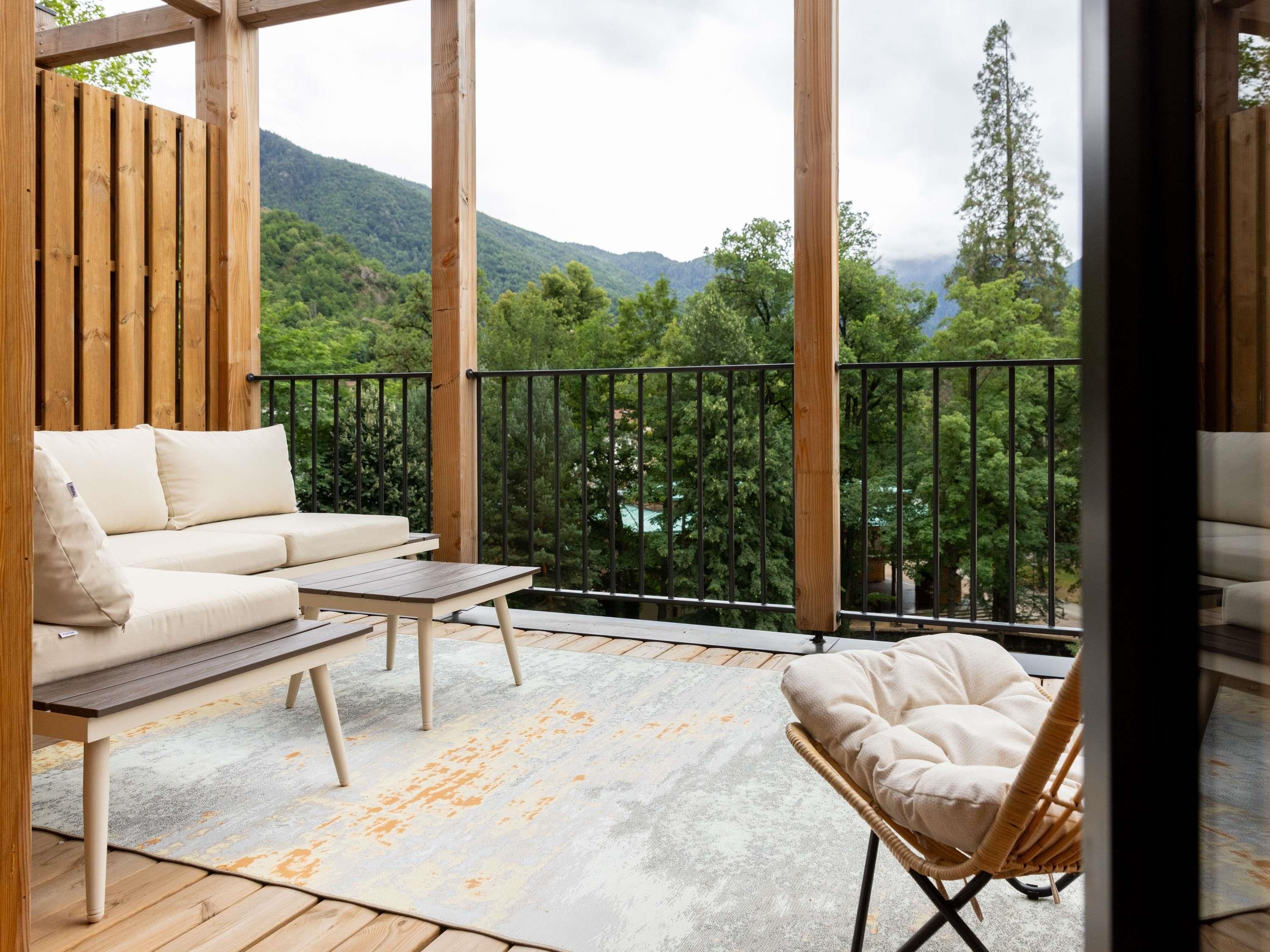 Un balcón con sofá, una silla y una mesa, con vistas a un paisaje montañoso.