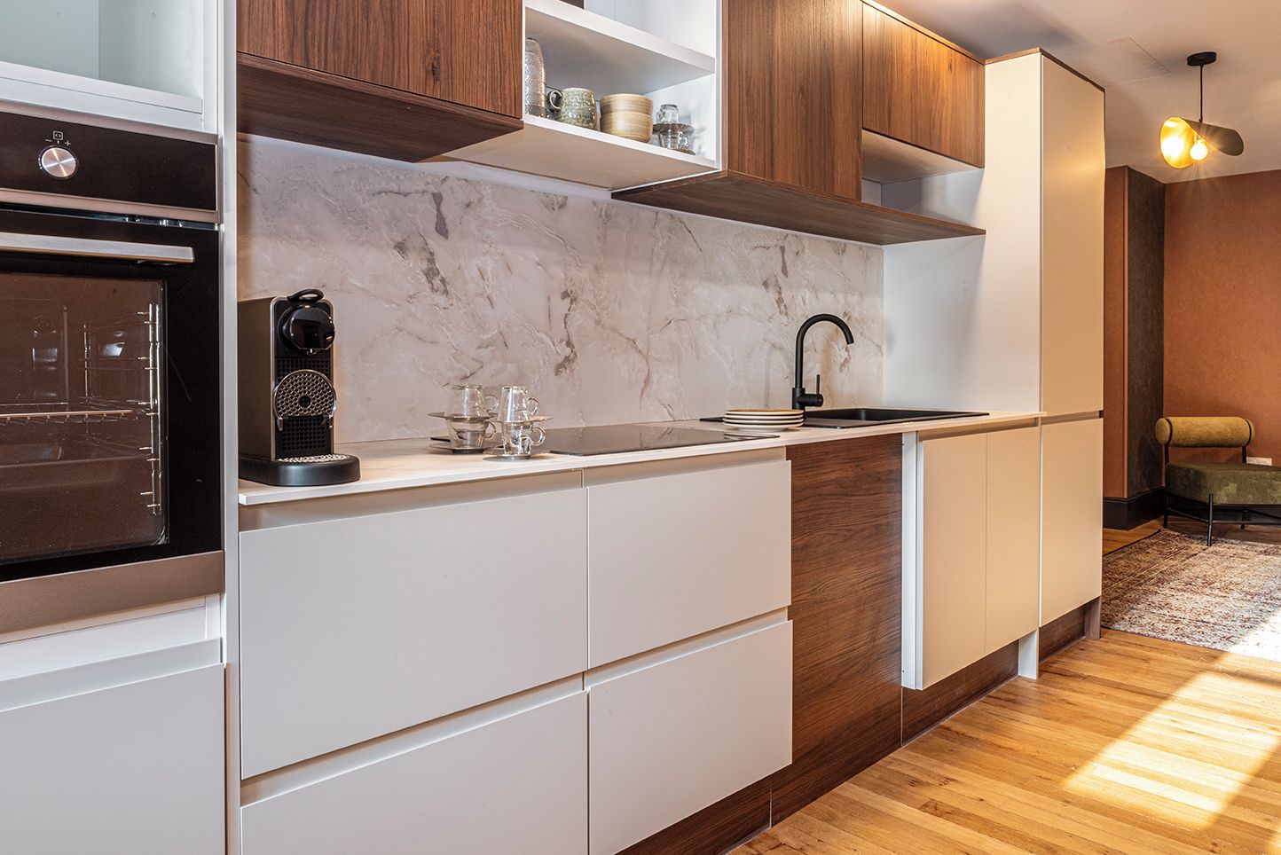 Una cocina moderna con armarios blancos, salpicadero de mármol y horno empotrado.