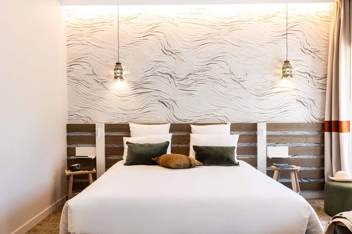 Ein Schlafzimmer mit Bett, Kissen, Nachttisch, Kamera und Lampe.