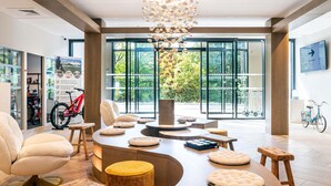 Un intérieur moderne avec un espace salon aux lignes courbes, un lustre et de grandes fenêtres offrant une vue sur l’extérieur.