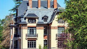 Un edificio de varios pisos con una fachada simétrica, varias chimeneas y un balcón con barandilla de hierro forjado.