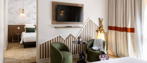 Una habitación de hotel con una cama, televisión, sillón verde, una mesita y una lámpara decorativa.