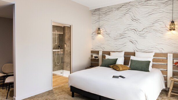 Un dormitorio moderno con una cama grande, un vestidor y una zona de ducha con mampara de vidrio.