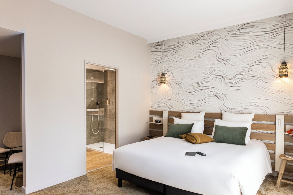 A modern bedroom with a large bed, a walk-in closet, and a glass shower area.