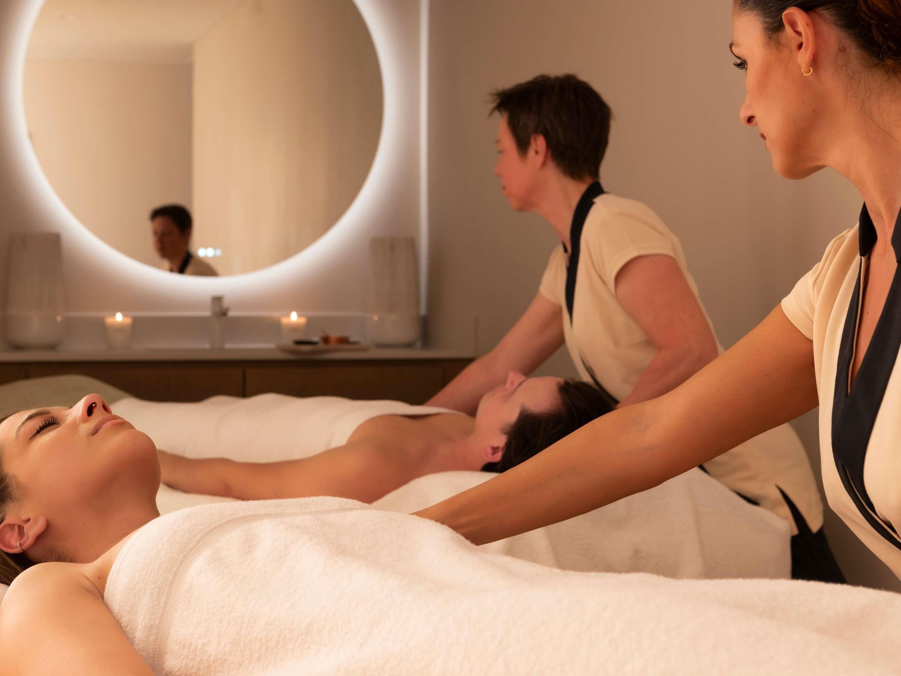 Ein Wellnessbereich mit Massageliege, großem Spiegel und Kerzen.