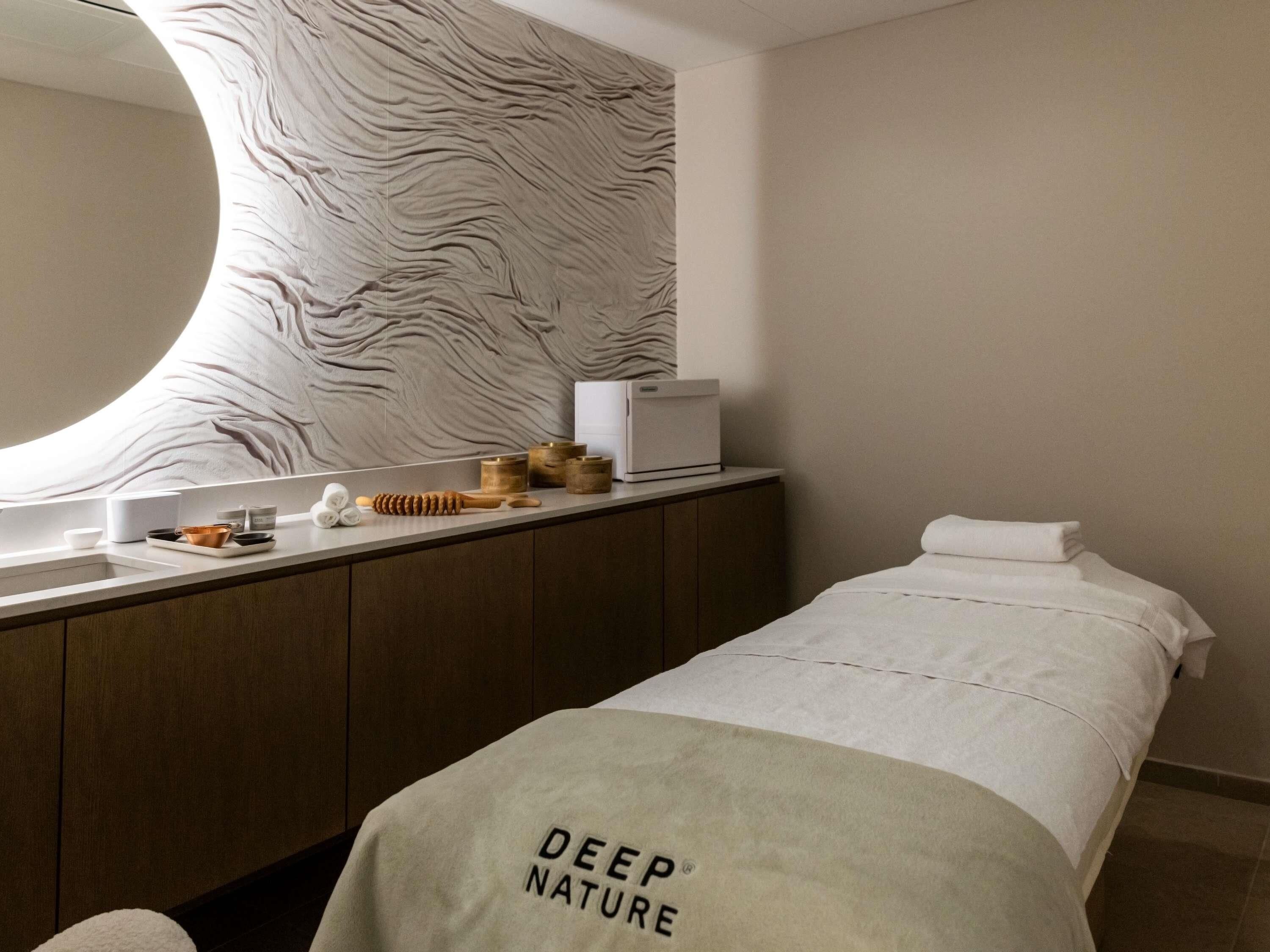 A modern hotel room with a large mirror, a wooden vanity, a bed with a white bedspread, and a wall with a textured pattern.