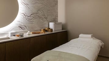 A modern hotel room with a large mirror, a wooden vanity, a bed with a white bedspread, and a wall with a textured pattern.