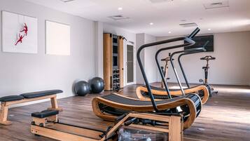 Un gimnasio moderno con máquinas de remo, pelotas de ejercicio y un banco.