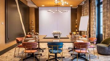 Uma sala de conferências com uma mesa grande, cadeiras, um projetor e um quadro branco.