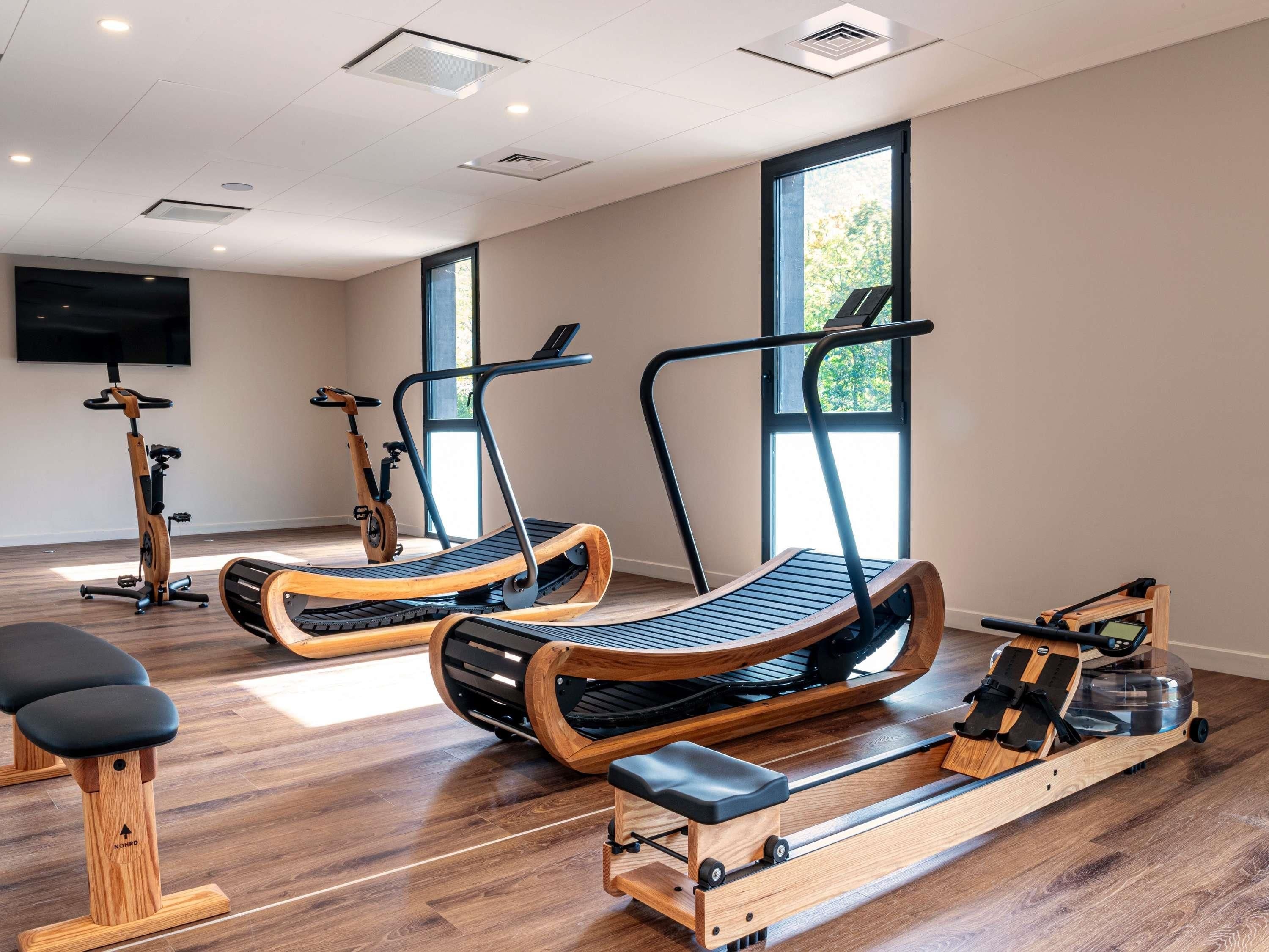 Ein Fitnessstudio mit Trainingsgeräten, großen Fenstern und einem Flachbildfernseher.