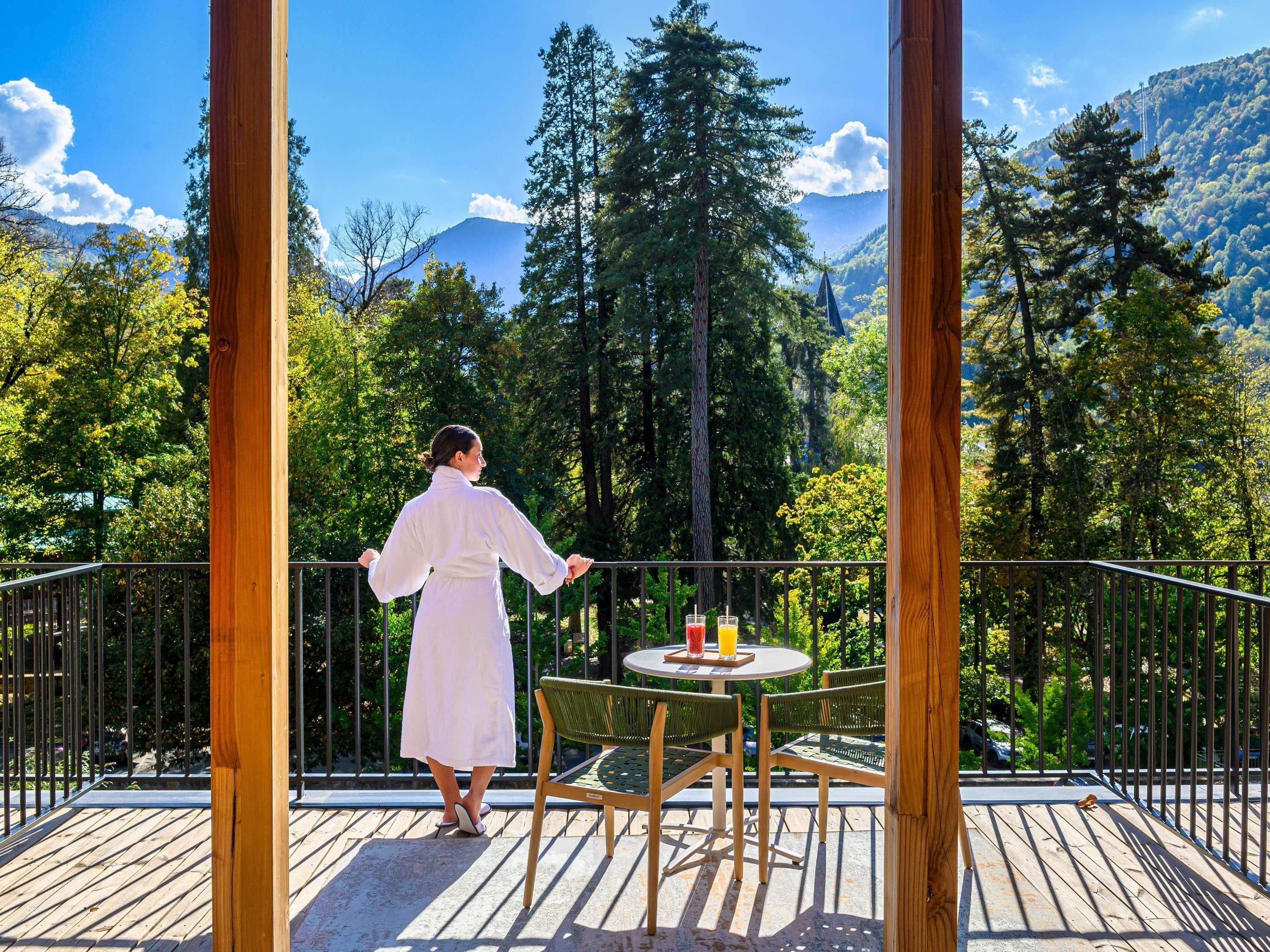 A person on a balcony overlooking a forested mountain area.