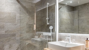 Un baño moderno con un espejo grande, un lavamanos blanco y una zona de ducha.