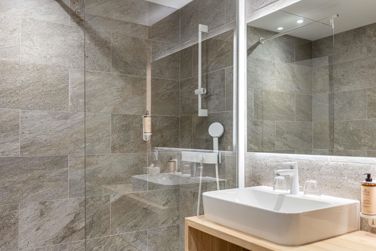 A modern bathroom with a large mirror, a white sink, and a shower area.