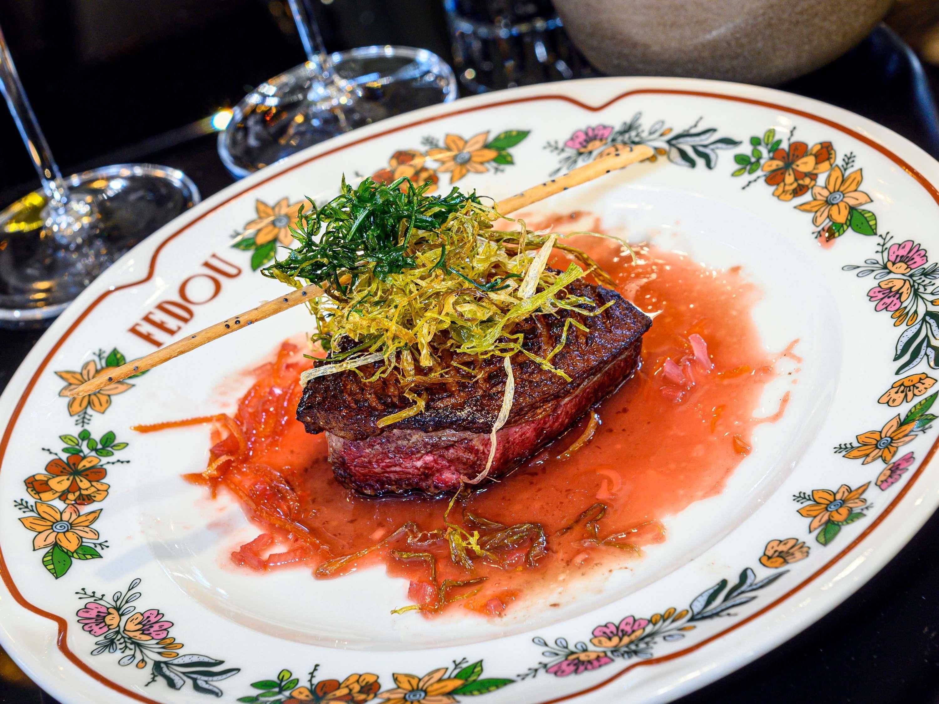 A plate with a steak, garnished with greens and thinly sliced onions, on a floral-patterned plate.