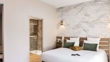 A modern hotel room with a large bed, a wooden headboard, and a glass-enclosed shower.