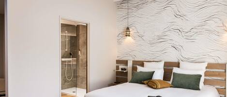 A modern hotel room with a large bed, a wooden headboard, and a glass-enclosed shower.