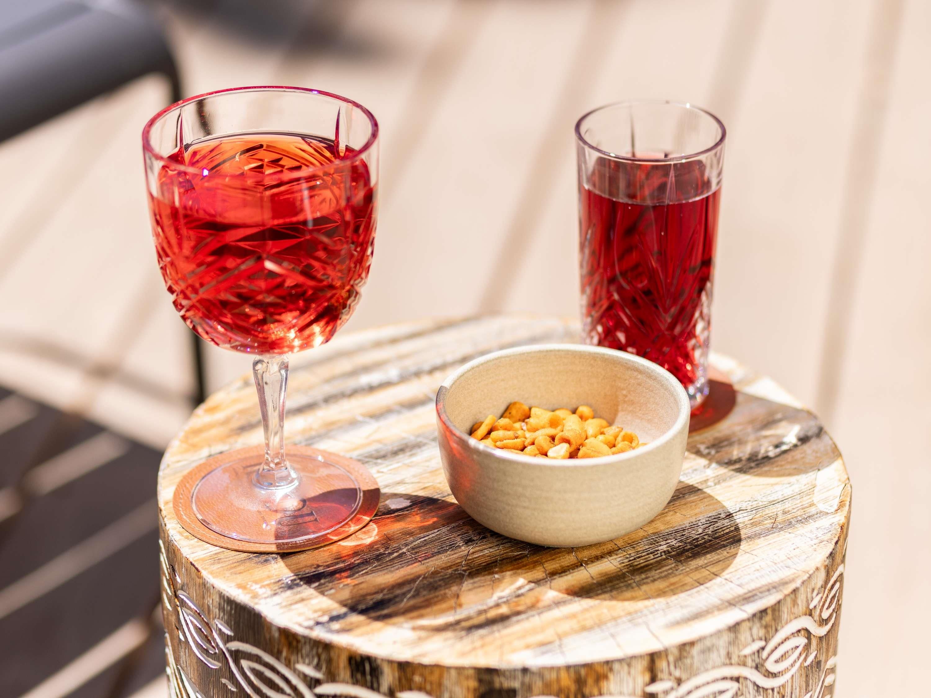Deux verres d’une boisson rouge sont posés sur une table en bois, à côté d’un bol de noix.