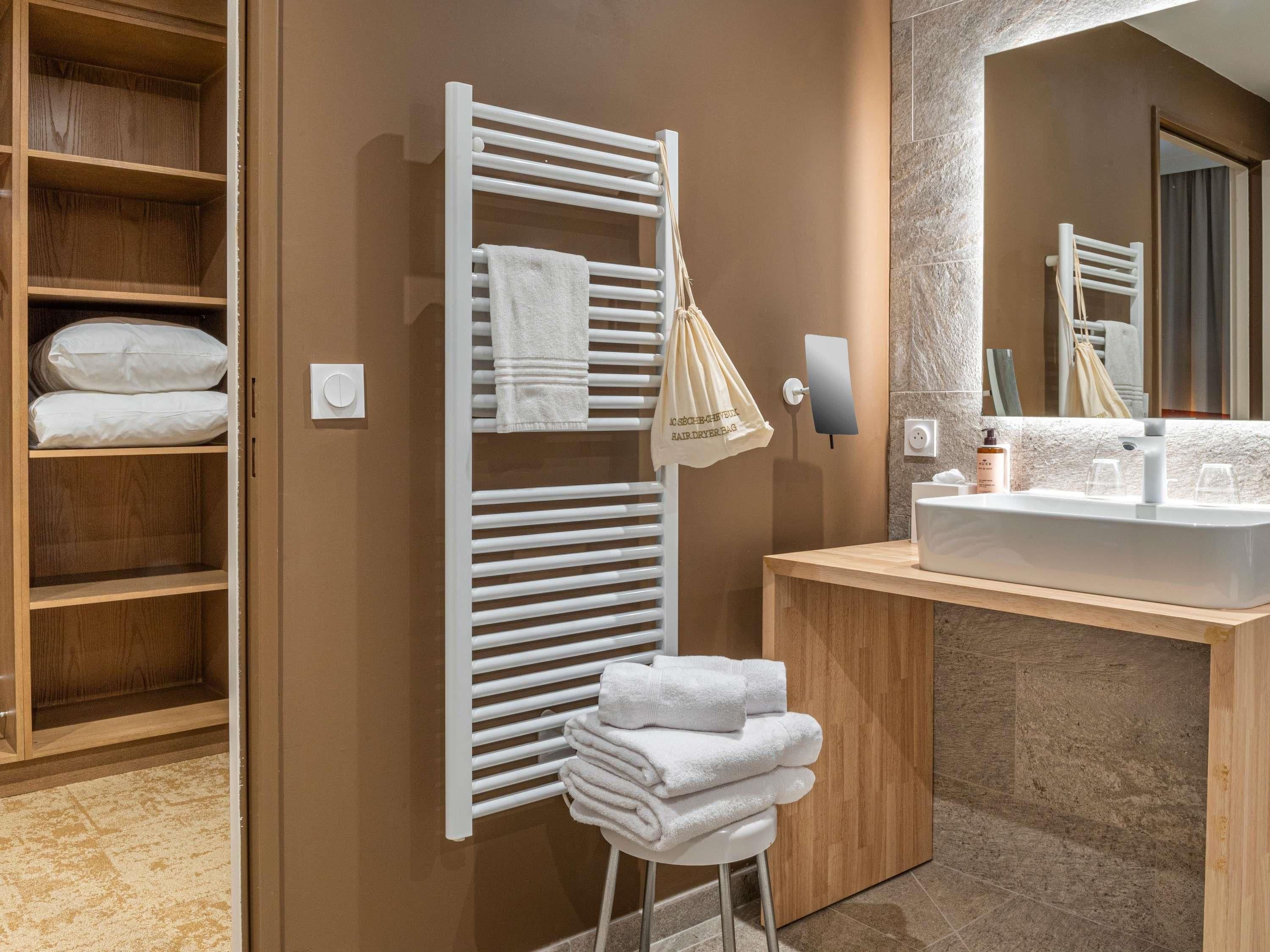 A modern bathroom with a wooden vanity, a towel rack with folded towels, and a mirror.