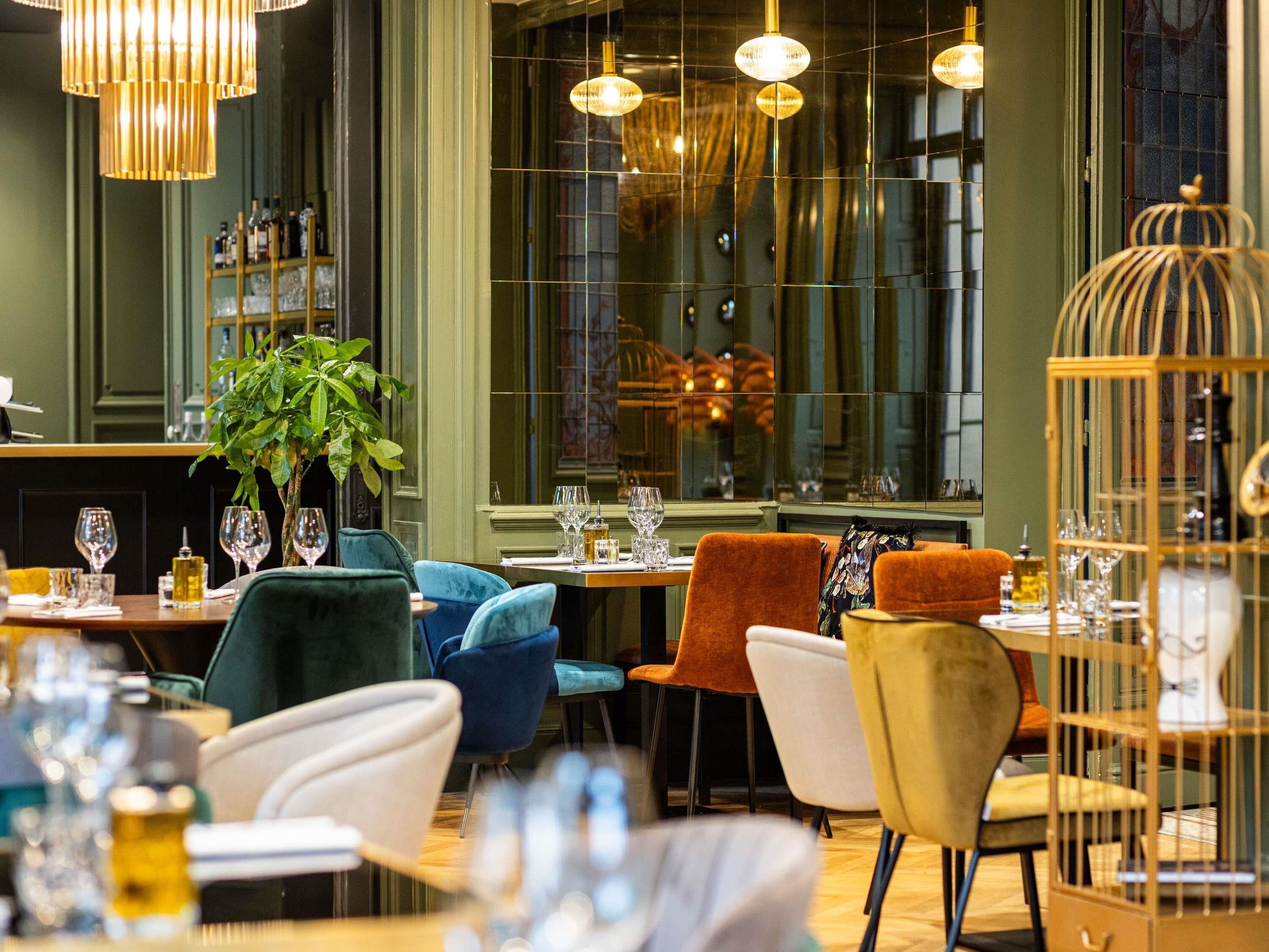 Een restaurantinterieur met gedekte tafels, stoelen, hangende lampen en een groot raam.