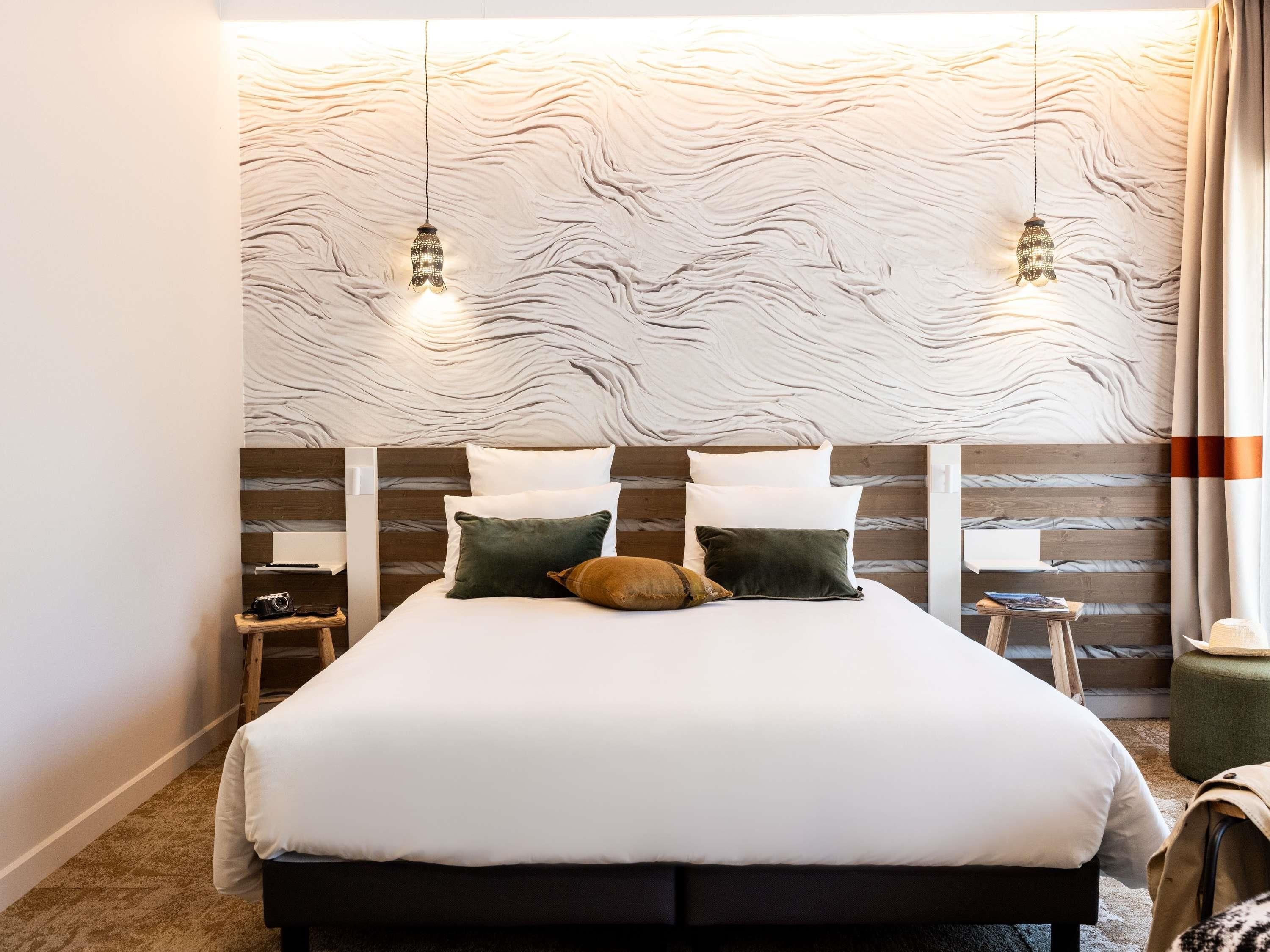 A bedroom with a bed, pillows, a nightstand, a camera, and a lamp.