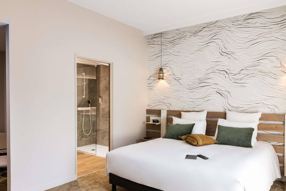 Ein modernes Hotelzimmer mit einem großen Bett, einem Holzkopfende und einer Duschkabine aus Glas.