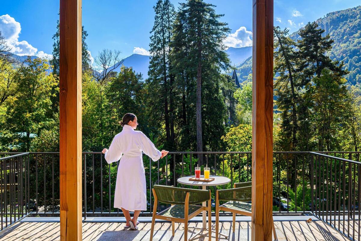 Eine Person auf einem Balkon mit Blick auf eine bewaldete Berglandschaft.