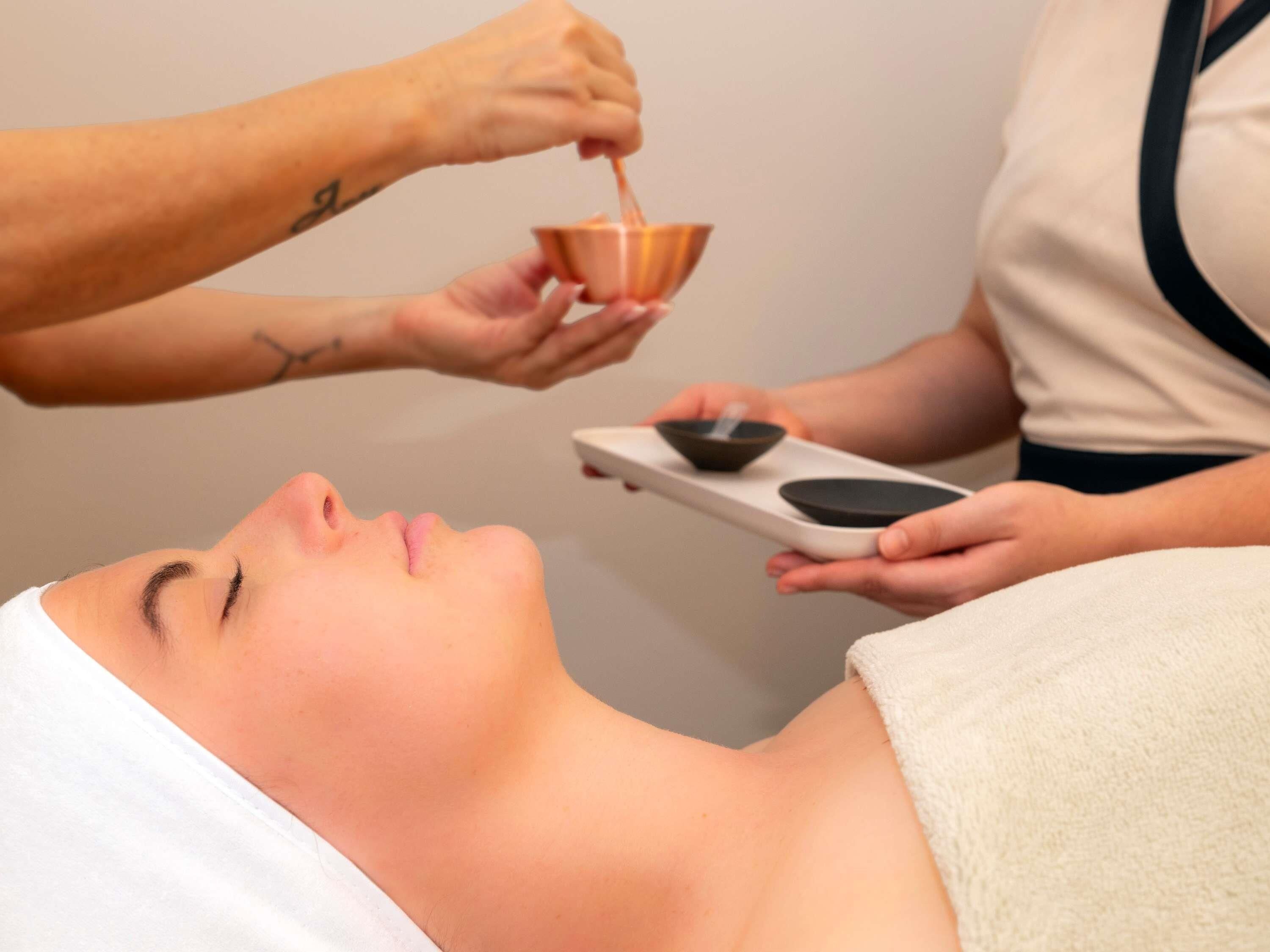 Une personne qui reçoit un soin du visage, avec un bol et un plateau à proximité.