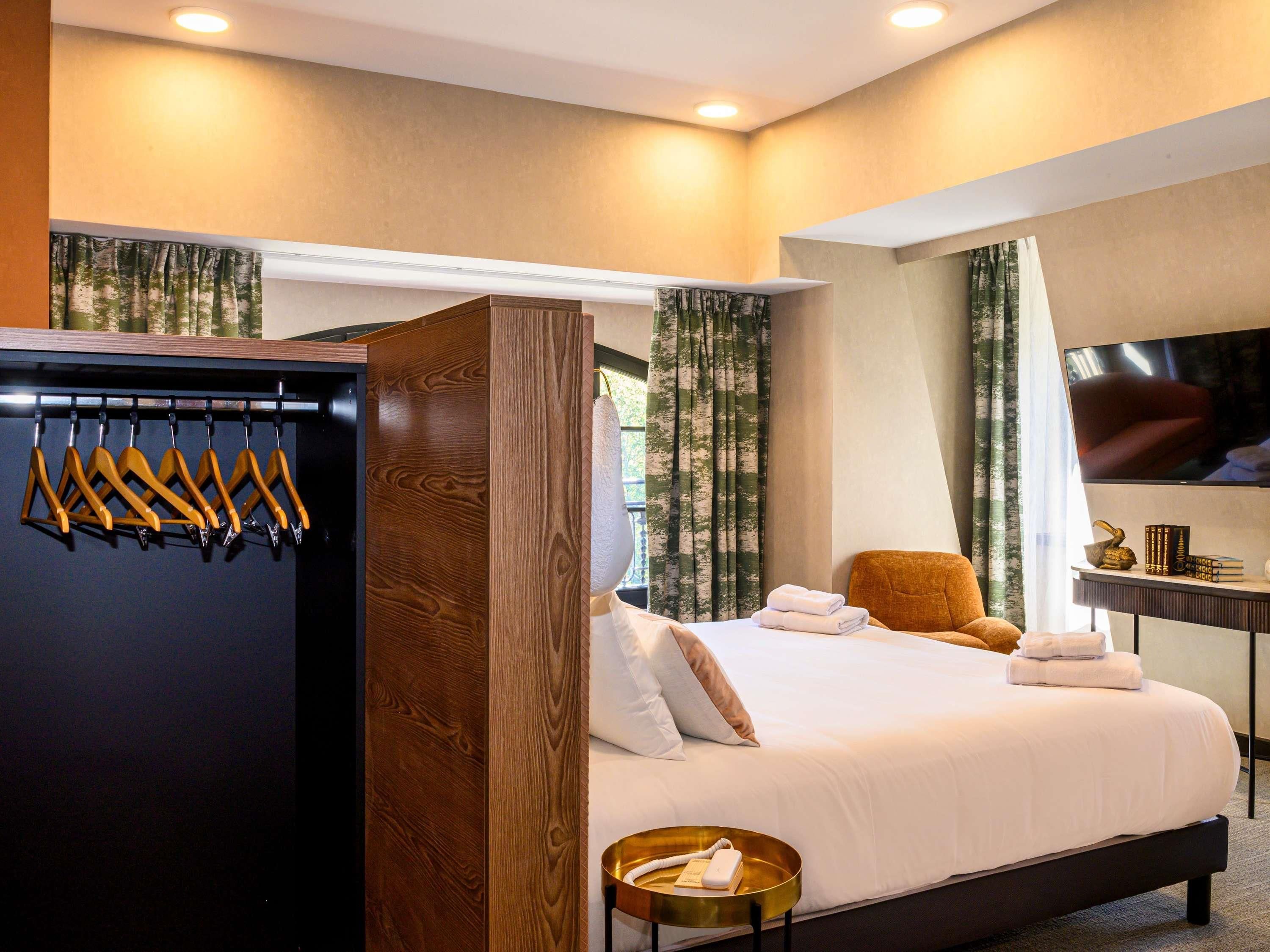 Una habitación de hotel con una cama, una silla, un televisor y un perchero.