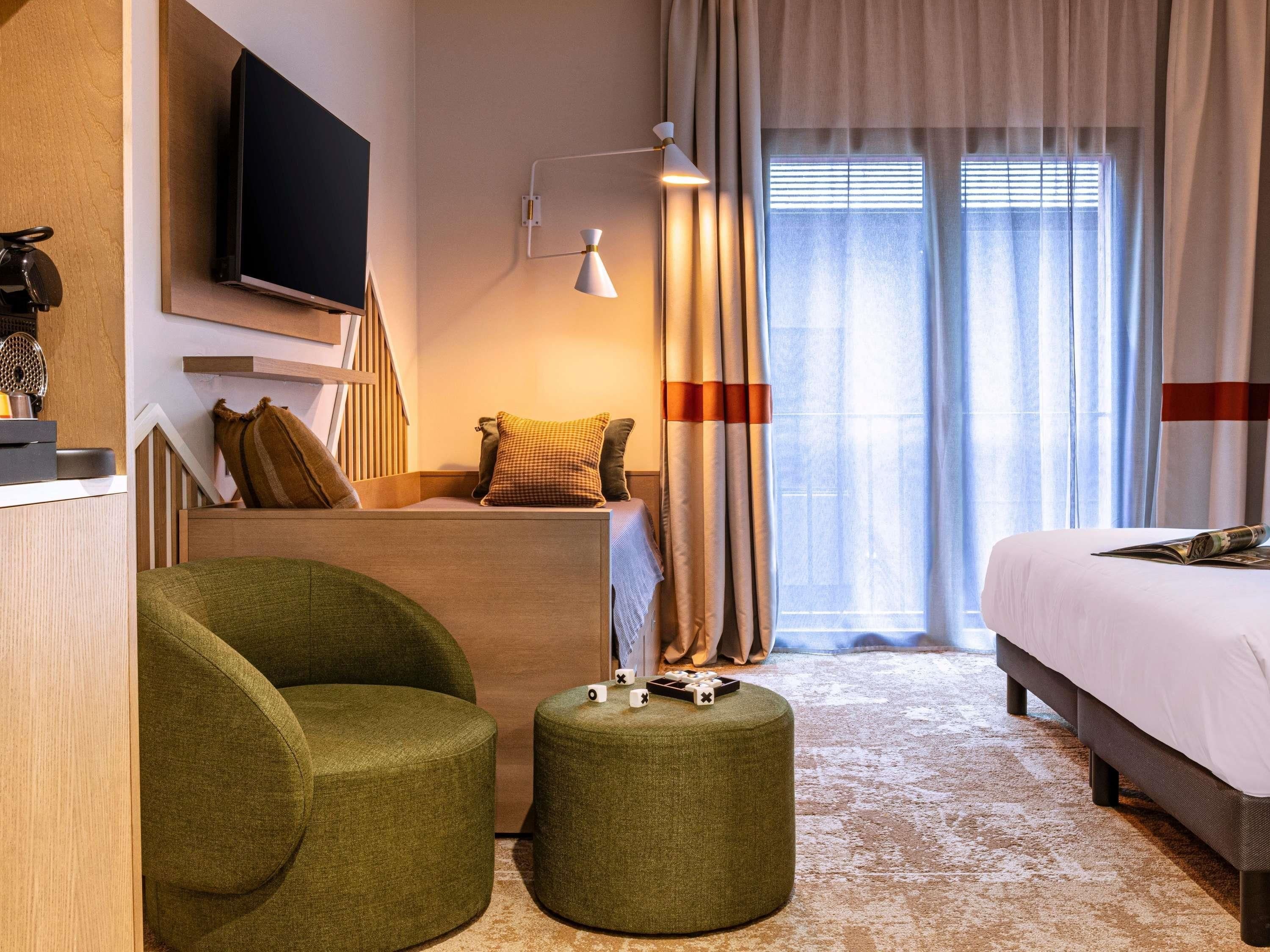 Une chambre d’hôtel équipée d’un lit, d’une télévision, d’un bureau, d’une chaise, d’une lampe et d’une fenêtre avec des rideaux.