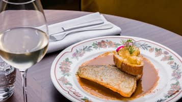 A plate with a fish dish and sauce, a glass of white wine, and a napkin with cutlery on a wooden table.