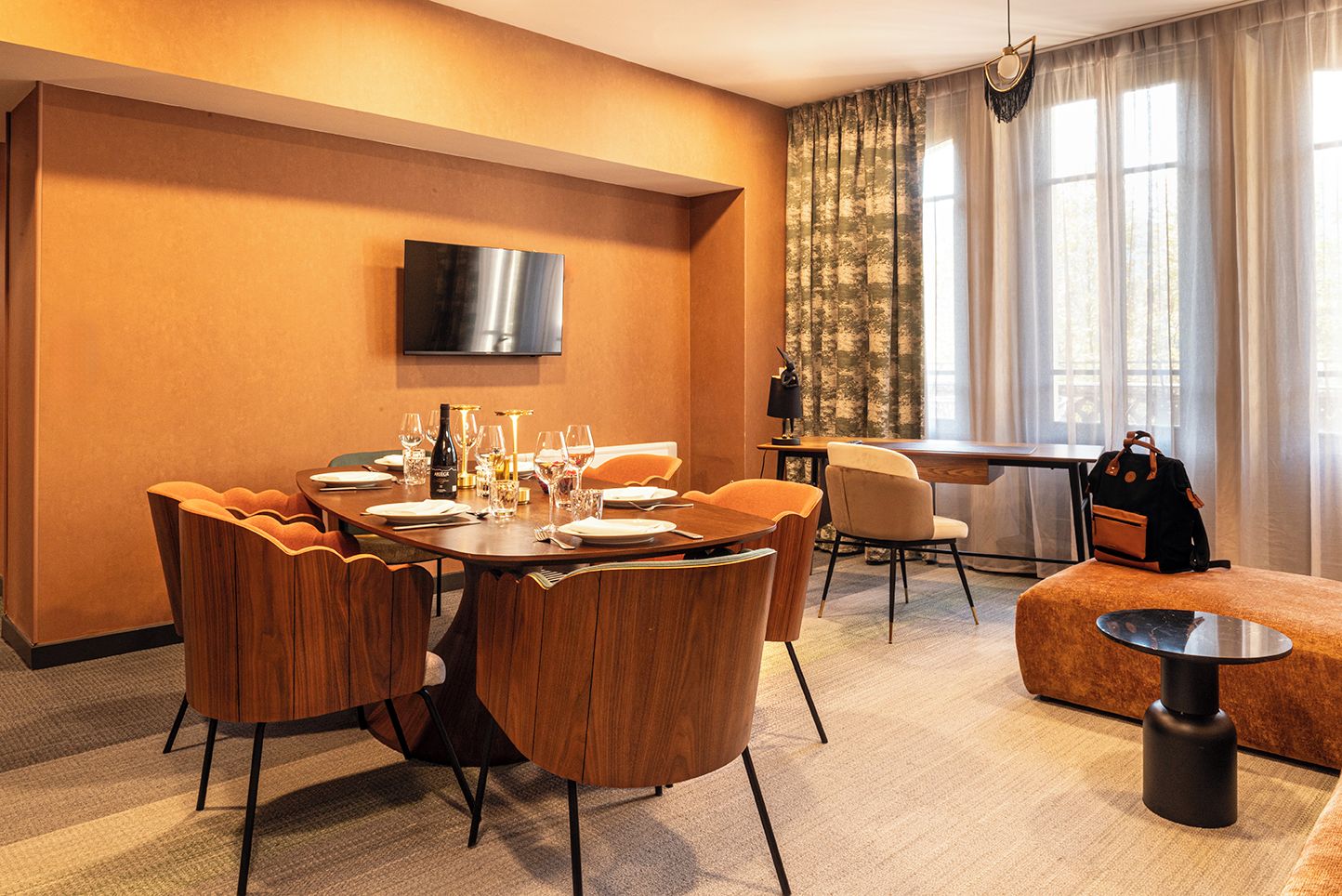 Une chambre d’hôtel comprenant un coin repas, un téléviseur fixé au mur, un canapé et une table sur laquelle se trouve un sac à dos.